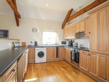 A kitchen with wooden cabinets black countertops a washing machine oven microwave and wooden ceiling beams at Tan Twr - Chellow Cottage in Dwyran