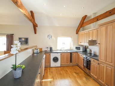 A kitchen with wooden cabinets and beams a washing machine and a microwave at Tan Twr - Chellow Cottage in Dwyran