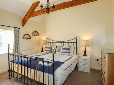 A bedroom with a metal bed frame two bedside tables with lamps a window and a wooden dresser at Tan Twr - Chellow Cottage in Dwyran