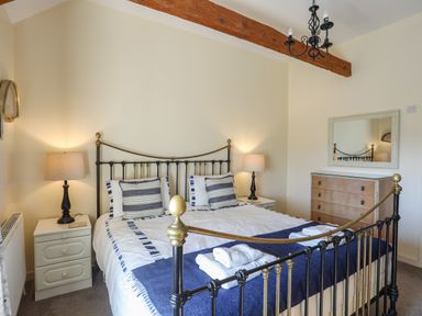 A bedroom with a metal bed frame bedside tables with lamps a chest of drawers and a wall mirror at Tan Twr - Chellow Cottage in Dwyran