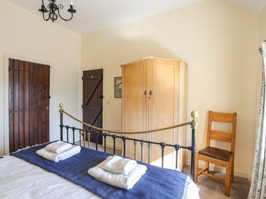 A bedroom with a metal bed frame and folded towels on the bed two wooden doors a wooden wardrobe and a wooden chair at Tan Twr - Chellow Cottage in Dwyran