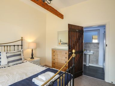 A bedroom with a bed a bedside table with a lamp a dresser and an open door showing a bathroom at Tan Twr - Chellow Cottage in Dwyran