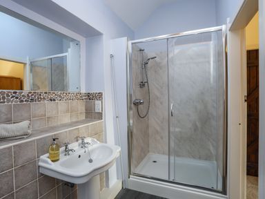A bathroom with a sink countertop mirror and a glass door shower at Tan Twr - Chellow Cottage in Dwyran