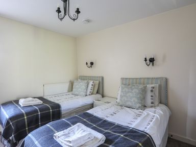 A bedroom with two single beds with blue plaid blankets and pillows at Tan Twr - Chellow Cottage in Dwyran