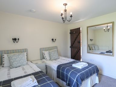 A bedroom with two single beds a large mirror on the wall and a wooden door at Tan Twr - Chellow Cottage in Dwyran