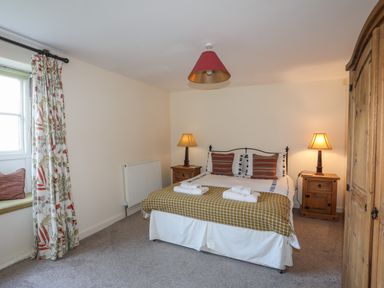 A bedroom with a double bed two bedside tables lamps a wardrobe and a window with curtains at Tan Twr - Chellow Cottage in Dwyran
