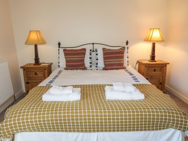 A bedroom with a double bed two bedside tables with lamps and folded towels at Tan Twr - Chellow Cottage in Dwyran