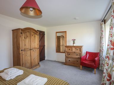 A bedroom with a wooden wardrobe chest of drawers and a red chair at Tan Twr - Chellow Cottage in Dwyran