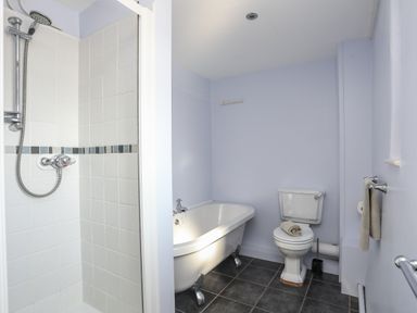 A bathroom with a shower, clawfoot bathtub, toilet with towel on top and towel rail on the wall at Tan Twr - Chellow Cottage in Dwyran