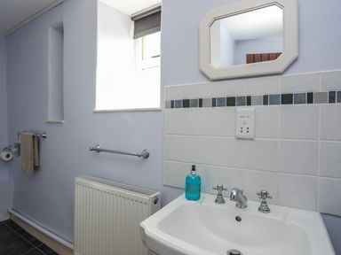 A bathroom with a sink a mirror a radiator and a window at Tan Twr - Chellow Cottage in Dwyran