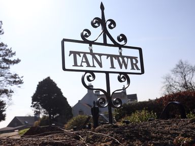 A decorative metal sign with the words TAN TWR mounted outdoors with buildings and trees in the background at Tan Twr - Chellow Cottage in Dwyran