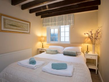 A bedroom with a double bed with rolled towels on it two bedside tables with lamps and a window at The Coach House - Beaumaris