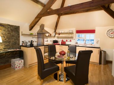 A kitchen with wooden beams glass dining table and black chairs at The Coach House in Beaumaris