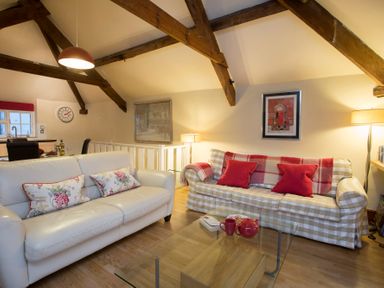 A living room with two sofas a glass coffee table and exposed wooden beams at The Coach House - Beaumaris