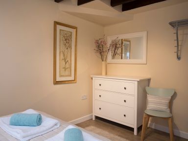 A bedroom corner with a white chest of drawers a mirror above a chair with a striped pillow and folded towels on a bed at The Coach House Beaumaris