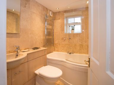 A bathroom with a toilet, sink, bathtub with glass shower screen, heated towel rail and a plant on the window sill at The Coach House - Beaumaris