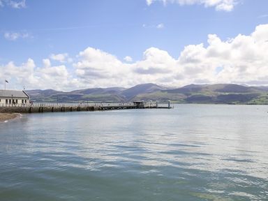 A pier extending into calm water with mountains and clouds in the background at The Coach House - Beaumaris