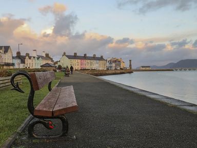 A waterfront promenade with benches along a paved path and row houses in the background at The Coach House - Beaumaris