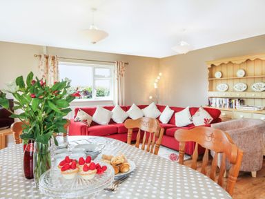 A dining table with flowers and pastries in a living room with a red sofa and wooden chairs at Coed Bolyn Lodge in Bethel