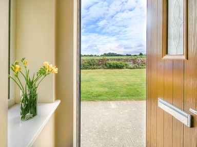 An open wooden door showing a concrete path and grass lawn with flowers in a glass vase on a white windowsill at Coed Bolyn Lodge in Bethel