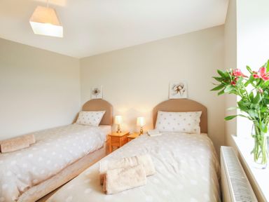 A bedroom with two single beds two bedside tables with lamps and a vase with flowers on the windowsill at Coed Bolyn Lodge in Bethel