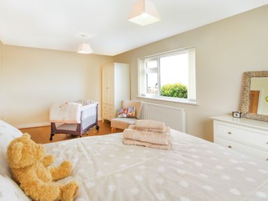 A bedroom with a bed with a teddy bear and towels on it a baby crib a chair a wardrobe a dresser with a mirror and a window at Coed Bolyn Lodge in Bethel