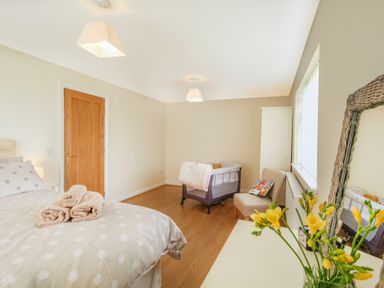 A bedroom with a bed and towels on it a baby crib a chair with a book a wooden door and a dresser with yellow flowers in a vase at Coed Bolyn Lodge in Bethel