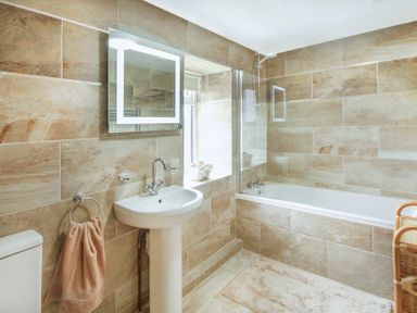 A bathroom with a toilet, pedestal sink with mirror, bathtub with shower, towel on holder, and a wicker chair at Coed Bolyn Lodge in Bethel