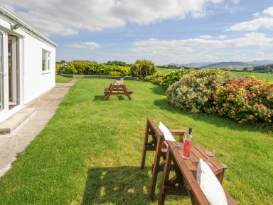 A garden with wooden benches and a picnic table outside a white building at Coed Bolyn Lodge in Bethel