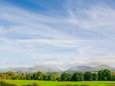A green field with trees and mountains in the background under a blue sky at Coed Bolyn Lodge in Bethel