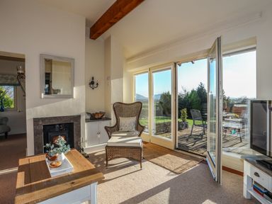 A living room with a fireplace wicker chair coffee table and glass doors opening to a patio at Cosy Barn in Llangaffo