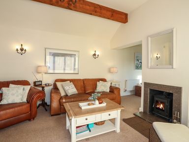 A living room with brown leather sofas a wooden coffee table a fireplace and lamps at Cosy Barn in Llangaffo