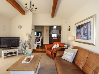 A living room with leather sofas a wooden coffee table tv and a view into a kitchen at Cosy Barn in Llangaffo