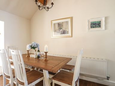 A dining room with a wooden table six chairs candles a vase of flowers and two framed pictures on the wall at Cosy Barn in Llangaffo