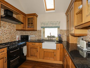 A kitchen with wooden cabinets black countertops a black stove a white sink and a window at Cosy Barn in Llangaffo