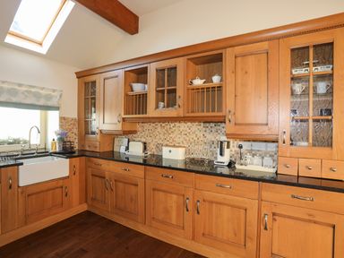 A kitchen with wooden cabinets black countertops a white farmhouse sink and kitchen appliances at Cosy Barn in Llangaffo