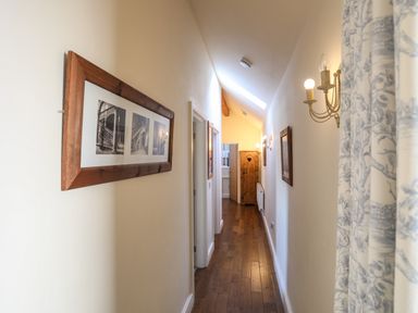 A narrow hallway with wooden floor and framed pictures on the wall at Cosy Barn in Llangaffo