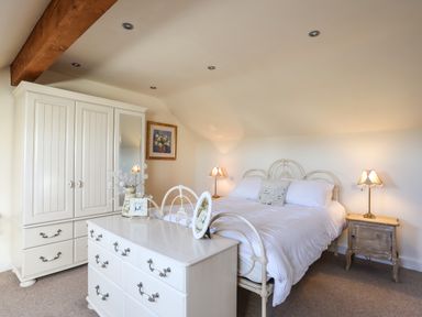 A bedroom with a white bed with a pillow a wooden wardrobe and a white dresser with framed photos at Cosy Barn in Llangaffo