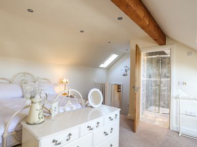 A bedroom with a bed white dresser a lamp and an open door leading to a bathroom at Cosy Barn in Llangaffo
