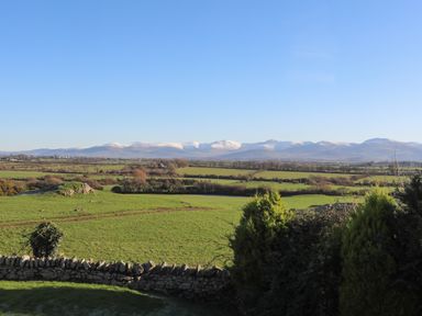 A rural landscape with green fields stone wall and snow capped mountains in the distance at Cosy Barn in Llangaffo