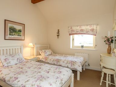 A bedroom with two single beds a bedside table with a lamp a window with floral blinds and a dressing table with a stool at Cosy Barn in Llangaffo