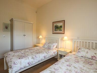 A bedroom with two single beds with floral bedspreads two bedside tables with lamps a wardrobe and a framed picture on the wall at Cosy Barn in Llangaffo