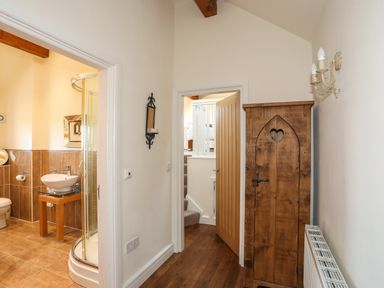 A hallway with a wooden cabinet and radiator next to a bathroom with a shower at Cosy Barn in Llangaffo