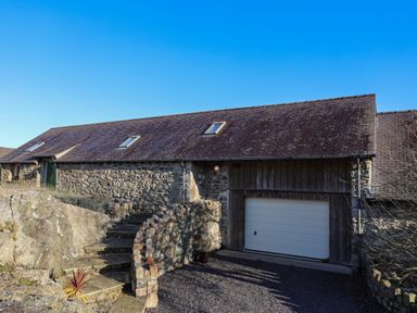 A stone building with a garage door and stone steps leading up to a green door at Cosy Barn in Llangaffo