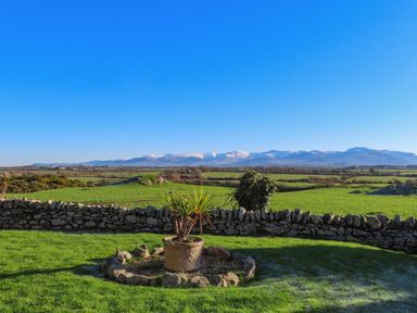 A garden with a stone wall and a potted plant overlooking green fields and distant snow-covered mountains at Cosy Barn in Llangaffo