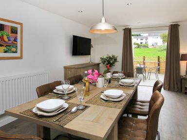 A dining room with a wooden table set for six and leather chairs leading to a patio at Cuckooland in Borth-Y-Gest