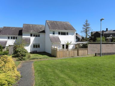 A white two-story house with a fenced patio and grassy yard under a clear blue sky at Cuckooland in Borth-Y-Gest