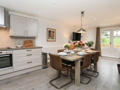 A kitchen and dining area with a set table on a wooden table and brown chairs at Cuckooland in Borth-Y-Gest