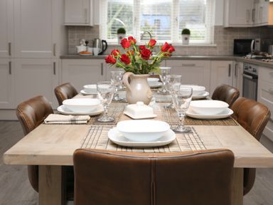 A dining table set with plates glasses and a vase of red roses in a kitchen at Cuckooland in Borth-Y-Gest