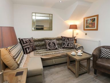 A living room with a beige sofa with patterned cushions and a wooden coffee table with cups and plates at Cuckooland in Borth-Y-Gest